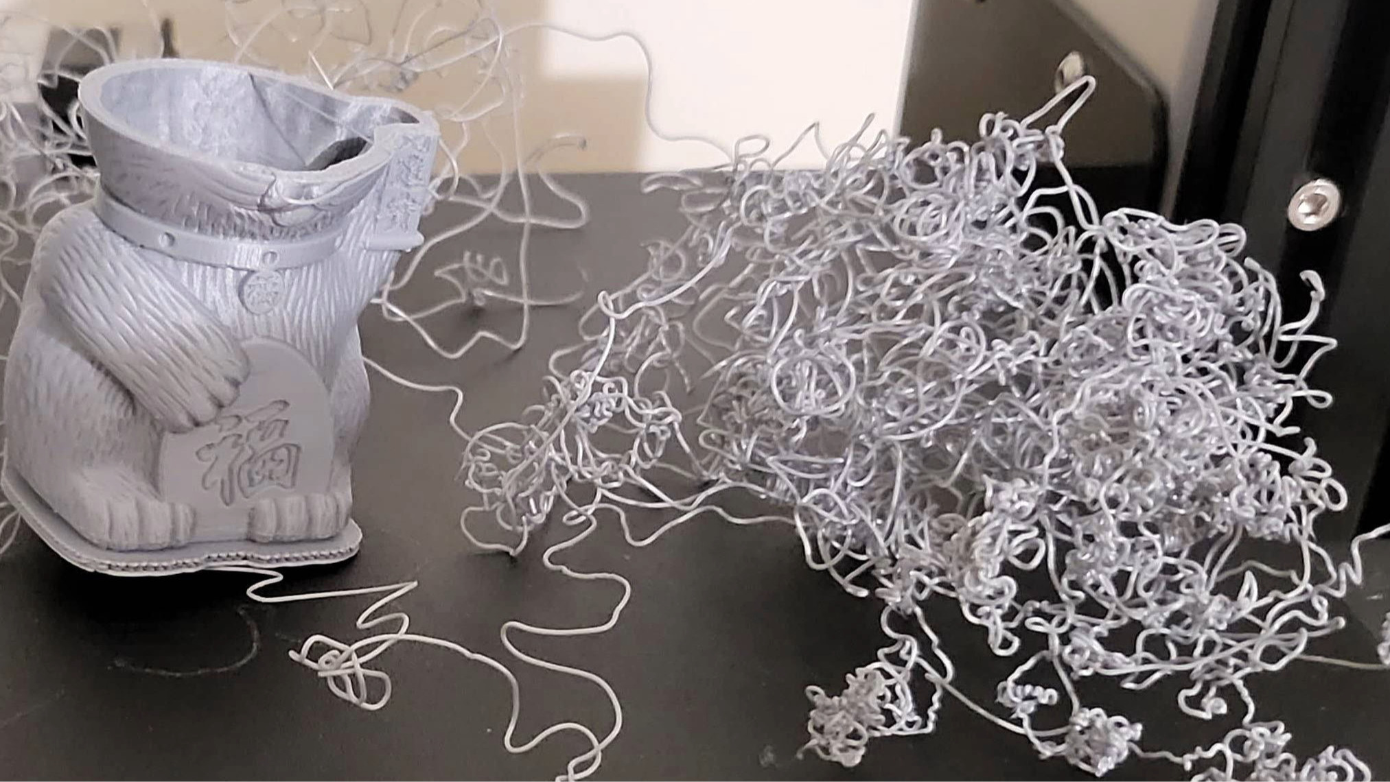 a failed 3D print with filament piling up next to a half-completed cat model